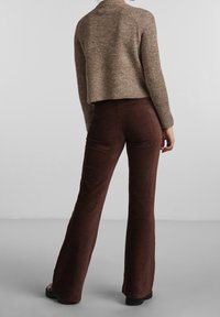 Brauner, gerippter Strickpullover mit einem cropped Design, kombiniert mit dunkelbraunen Cordhosen mit weit ausgestelltem Bein, die eine strukturierte Oberfläche und eine hohe Taille aufweisen.