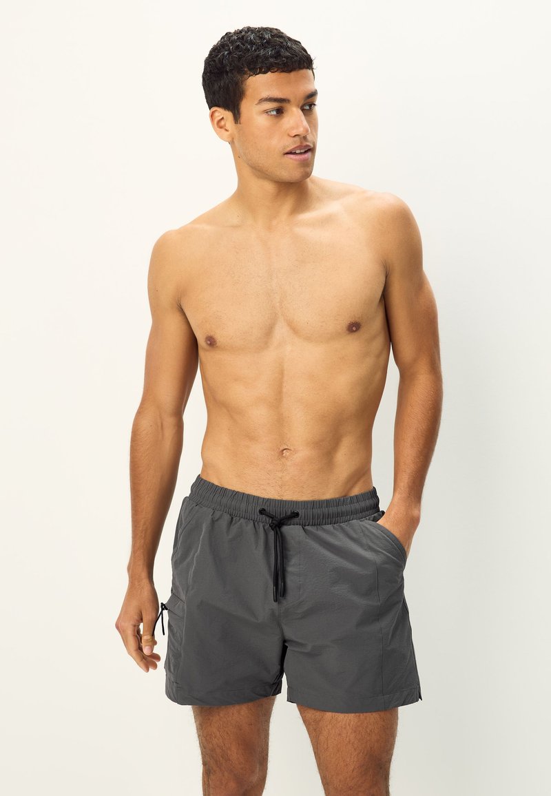 Heren zwemshorts in donkergrijs, gemaakt van lichtgewicht stof. Voorzien van een elastische tailleband met trekkoord, zijzakken en een casual pasvorm.