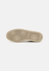 Beige gummisåle med sirkulære og teksturerte mønstre, med rygger langs kantene for grep og feste.