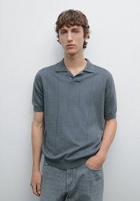 Gray knitted polo shirt with short sleeves, a collar, and vertical ribbed texture. Paired with light gray, loose-fit jeans.