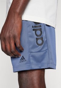 Modré sportovní kraťasy vyrobené z strukturované látky. Mají velké černé logo 'adidas' na jedné straně a menší černé logo blízko lemu.