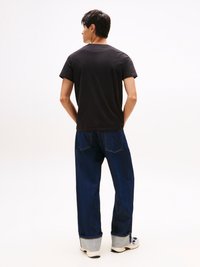 Svart bomull T-skjorte med rund hals. Iført med løs passform mørkeblå denimjeans med oppbrettede hem og baklommer.