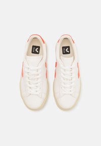 Hvite lær sneakers med oransje detaljer, flate lisser og gummisåle. Logoen er synlig på innersålen og tungen.