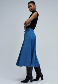 Denim A-linje kjol i medelblått med hög midja, knapppatron och en flödande, full silhuett. Matchad med åtsittande svarta stövlar.