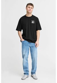 Sort bomulds T-shirt med korte ærmer og grafik på fronten. Lyseblå denim jeans; grå sneakers med tre striber detaljer.
