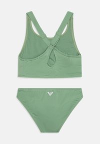 Grünes zweiteiliges Bikini aus Textil mit strukturierter Oberfläche. Das Oberteil hat ein Racerback-Design und ein Schlüssellochdetail; die Unterteile sind schlicht mit einem Logo-Accent.