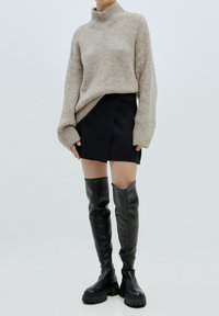 Beige gebreide coltrui met lange mouwen, gecombineerd met een zwarte mini-jurk en zwarte leren kniehoge laarzen met dikke zolen.