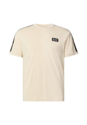 Krämfärgad t-shirt i mjuk bomull, med korta ärmar, en svart logopatch på bröstet och svarta ränder längs axlarna.