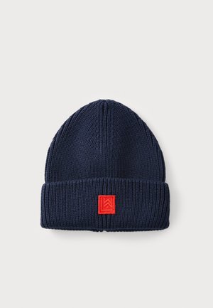 Berretto lavorato a maglia di colore blu navy con orlo ripiegato e una toppa quadrata rossa con un design geometrico. Texture a coste.