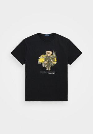 Melnā kokvilnas T-kreklā attēlots lācis zaļā apģērbā blakus dzeltenam transportlīdzeklim, apakšā teksts "POLO BEAR by RALPH LAUREN".