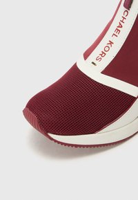 Sneaker bordeaux con tomaia in rete, dettagli bianchi e suola testurizzata. Presenta una punta liscia e dettagli di branding sul lato.