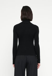 Čierny rolák z mäkkej látky, s dlhými rukávmi a priliehavým strihom, zobrazený zozadu na jednoduchom pozadí.