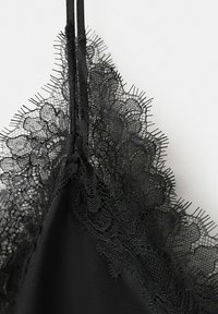 Gros plan sur un tissu noir bordé de dentelle avec des motifs floraux et une fine bretelle sur un fond clair.