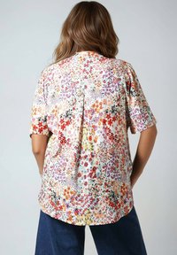Floral-patterned shirt in lightweight fabric, featuring short sleeves, a relaxed fit, and a pleat detail at the back. Colors include pink, red, and green.