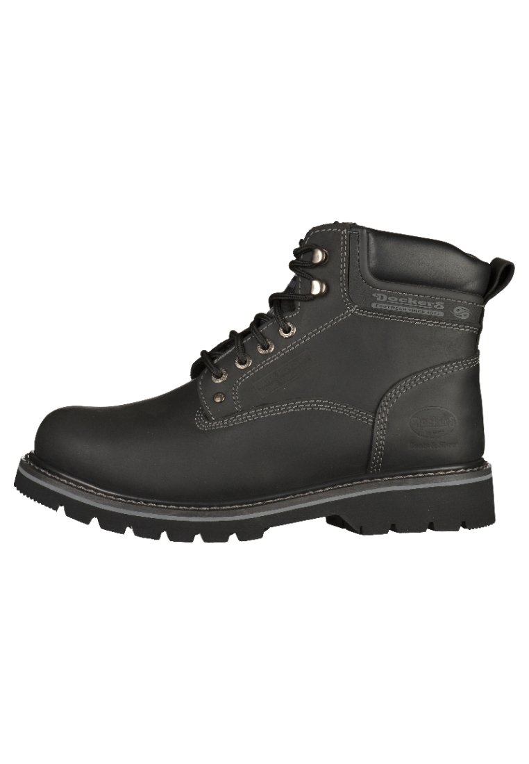 Botas de trabajo de cuero negro con un diseño robusto, puntera reforzada, ojales de metal y una suela gruesa y resistente. Detalles de costura en contraste presentes.