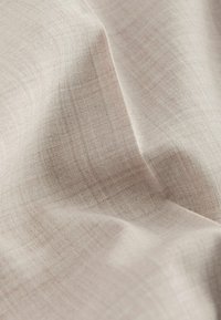 Tissu en lin beige clair avec une texture tissée subtile et des plis doux créant des ombres délicates.