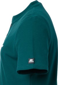Camisa polo de algodón en color verde azulado con un cierre de tres botones. Presenta mangas cortas y una etiqueta con el logo en la manga izquierda. Tejido texturizado.