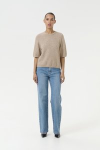Maglione beige a maniche corte con collo rotondo, abbinato a jeans dritti azzurri chiari. L'outfit ha una consistenza morbida e una vestibilità informale.