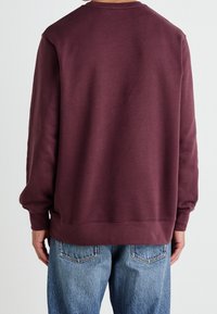 Burgundyröd sweatshirt med rund halsringning, långa ärmar och ribbad fåll. Kombinerad med ljusblå slitna jeans för kontrast.