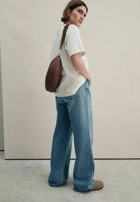 Helles Oversize-T-Shirt, hellblaue weite Jeans und eine braune Tasche mit Schultergurt, vor einem minimalistischen Hintergrund.