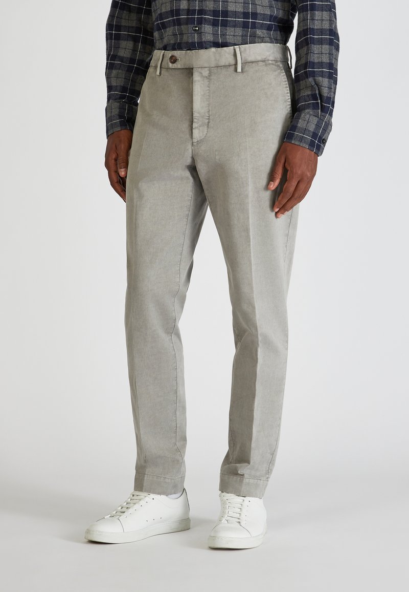 Pantalones gris claro con una textura suave, corte recto y detalles en los bolsillos frontales. Combinados con zapatillas blancas y una camisa a cuadros.