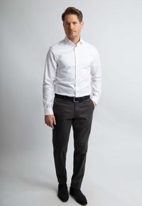 Witte overhemden met knopen, donkergrijze broek en zwarte laarzen. Het overhemd heeft lange mouwen en de outfit is netjes aangesloten met een riem.