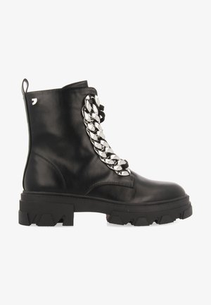 Bota de tobillo de cuero negro con una suela gruesa, que presenta un destacado acento de cadena de plata en la parte frontal y una pestaña de agarre en la parte trasera.