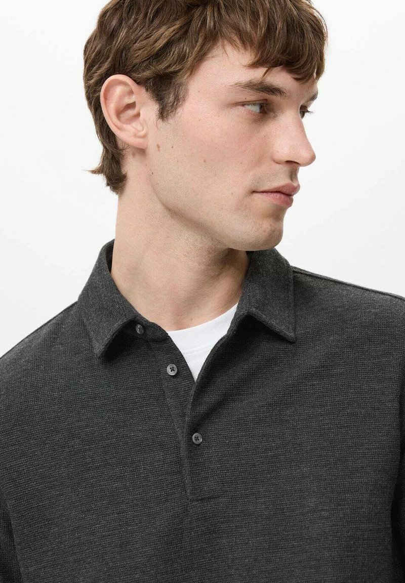 Dunkelgraues, strukturiertes Polohemd mit Kragen, drei Knöpfen und klassischem Schnitt, getragen über einem weißen T-Shirt.