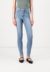 Jean skinny en denim bleu clair avec une taille haute. Assortis à des ballerines noires avec des accents de quincaillerie décoratifs.