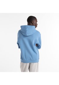 Sudadera con capucha en azul claro, confeccionada con tela suave. Ajuste holgado con dobladillo y puños elásticos. Sin logotipos ni patrones visibles.