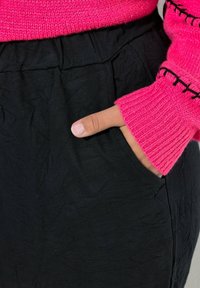 Czarne spodnie teksturowane z boczną kieszenią, zestawione z jasnoróżowym swetrem z dzianiny z prążkowanymi mankietami i dekoracyjnym przeszyciem.