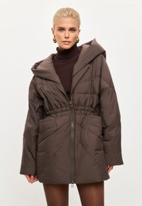 Bruine pufferjack met een ritsluiting, elastische tailleband en capuchon. Voorzien van een doorgestikt ontwerp en twee voorzakken. Glad, gevoerd materiaal.
