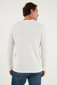 Langarmiges weißes Rippshirt mit Rundhalsausschnitt, aus strukturiertem Stoff und mit geradem Saum, kombiniert mit blauen Jeans.