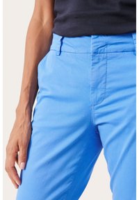 Ljust blå, bomullbyxor med fickor och bälteshällor, som har en slät yta och rak passform. Synliga sömnadsdetaljer finns.