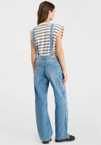 Lichte blauwe denim salopette met wijde benen, verstelbare banden en voorkruiszakken; gedragen over een gestreept T-shirt met korte mouwen.