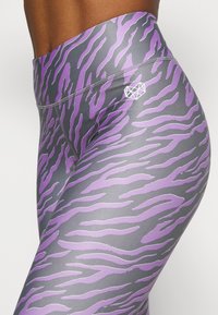 Leggings featuring a gray base with bold purple tiger stripe patterns. High-waisted design with a small white logo accent on the side.
