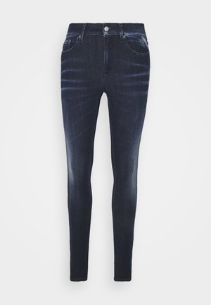 Dark blue denim skinny jeans with a smooth texture, featuring five pockets and a front button closure. Faded detailing along the legs.