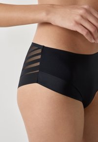 Schwarze Hipster-Shorts aus glattem Hauptmaterial mit transparenten, gestreiften Mesh-Akzenten an den Seiten. Das Design ist figurbetont und leicht.