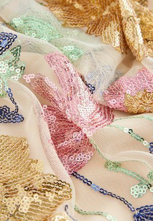 Tissu en maille beige avec des motifs floraux en sequins colorés dorés, roses, verts et bleus. Caractérisé par des textures superposées et des détails complexes.