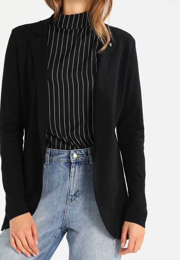 Blazer negro de tejido suave con frente abierto, combinado con un cuello alto de rayas negras y blancas. Vaqueros de mezclilla claros de tiro alto.