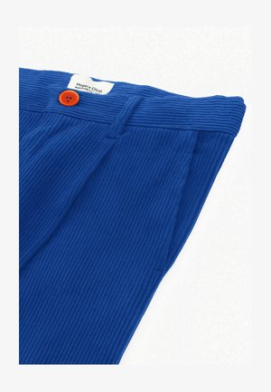 Blaue gerippte Hosen mit einem leuchtend orangefarbenen Knopf und sichtbarem Etikett am Bund vor einem weißen Hintergrund.