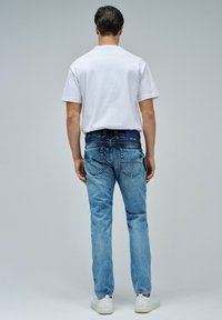 Camiseta de algodón blanca combinada con jeans de mezclilla azul desgastados. Los jeans tienen un diseño clásico de cinco bolsillos y son ligeramente ajustados. Zapatillas blancas.