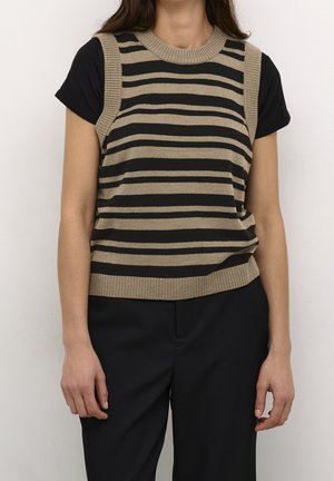 Femme portant un t-shirt noir à manches courtes avec un gilet en tricot sans manches beige et noir à rayures horizontales et un pantalon noir.