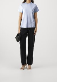 Světle modré bavlněné tričko s kulatým výstřihem, doplněné černými džíny s vysokým pasem. Modelka drží malou černou kabelku s texturovaným designem.