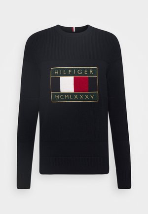 Granatowy sweter dzianinowy z wyraźnym haftowanym logo Hilfiger w prostokątnym wzorze z czerwonymi, białymi i niebieskimi akcentami.