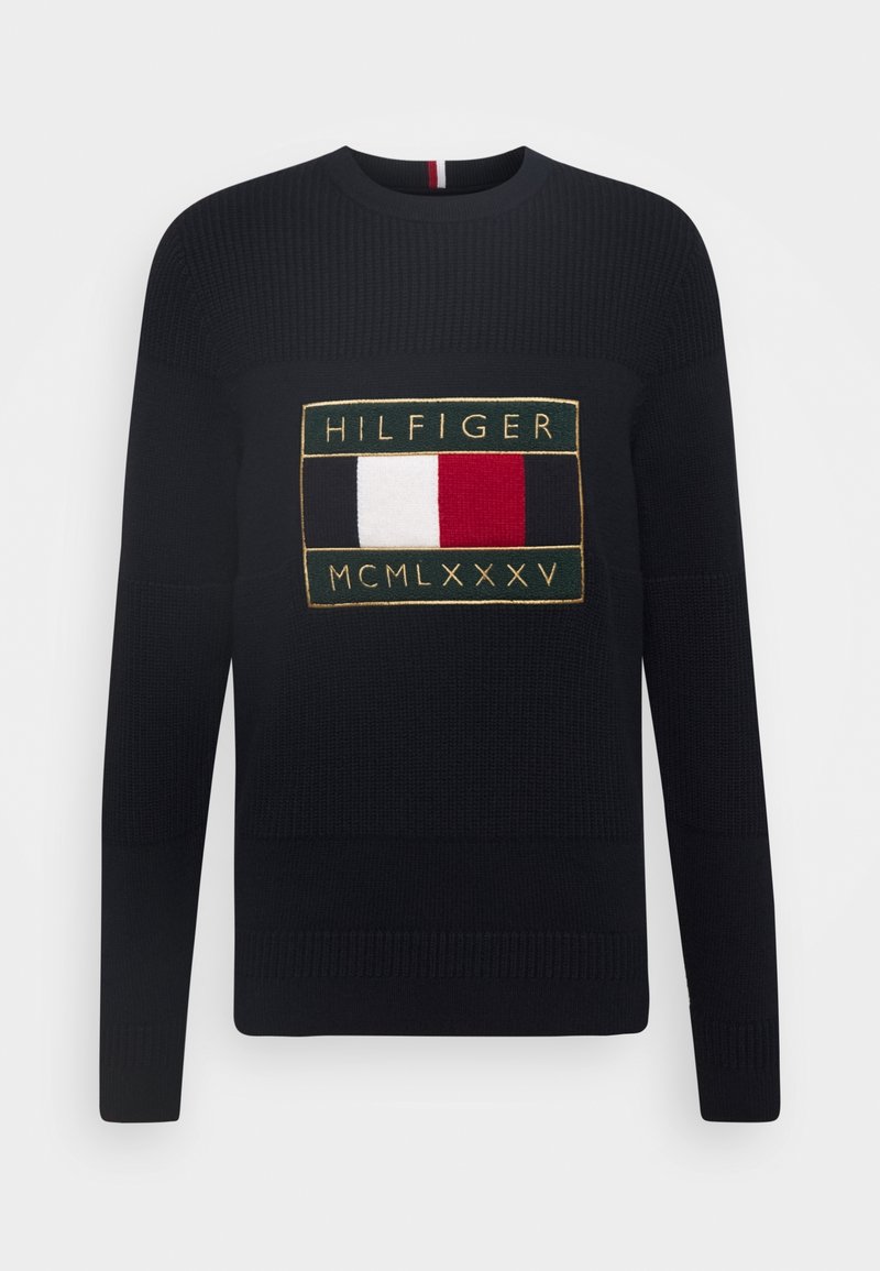 Granatowy sweter dzianinowy z wyraźnym haftowanym logo Hilfiger w prostokątnym wzorze z czerwonymi, białymi i niebieskimi akcentami.