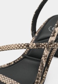 Sandalo con tacco alto con motivo in pelle di serpente beige e marrone, caratterizzato da sottili cinturini neri e una soletta imbottita per il massimo comfort.