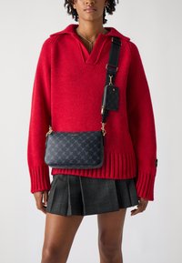 Knitted red sweater with a collar, black crossbody bag with a patterned texture, and a pleated gray plaid skirt. Gold hardware accents.