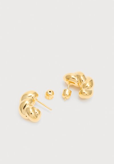 Ζευγάρι λαμπερά χρυσά στριφτά σκουλαρίκια με σχήμα κρίκου και πεταλούδα κλείσιμο πάνω σε ανοιχτό γκρι επιφάνεια.