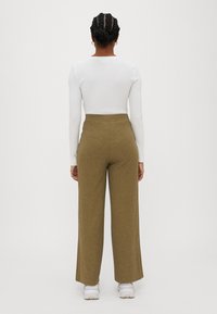 Långa, olivgröna, ribbade vida byxor som matchas med en figurnära vit långärmad topp. Outfiten fulländas med vita sneakers.